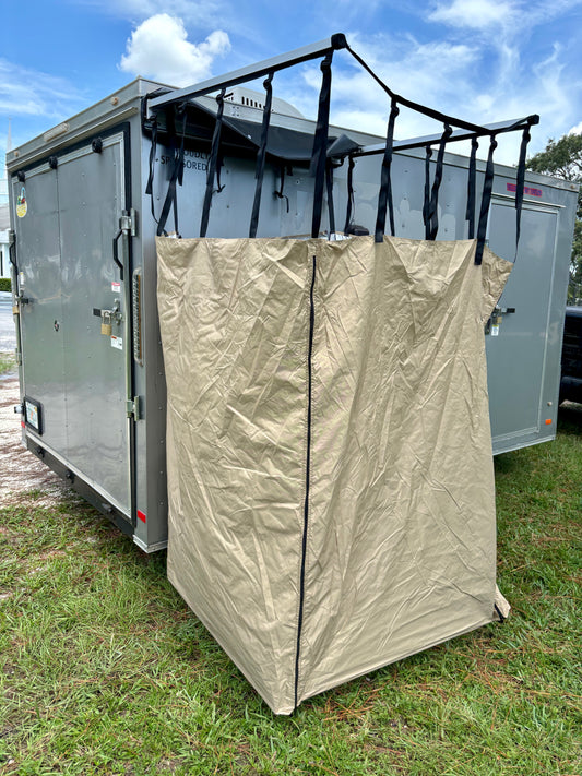 A beige fold-out privacy changing room shower tent mounted on the side of a vehicle, with adjustable straps and a visible storage bag.